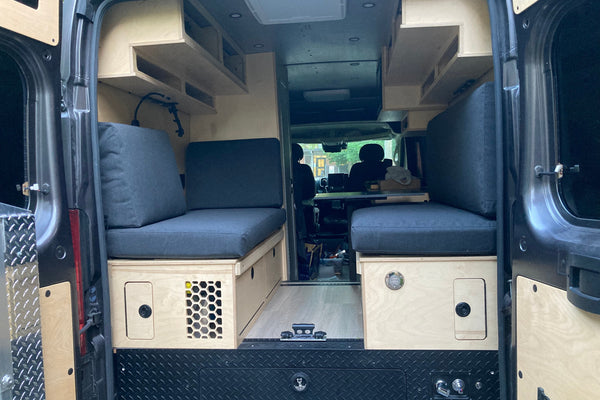 Rear view of a custom 2020 Ram ProMaster 2500 High Roof camper van with handcrafted birch cabinetry, bench seating, upper cabinets, and custom storage by Overland Interiors.