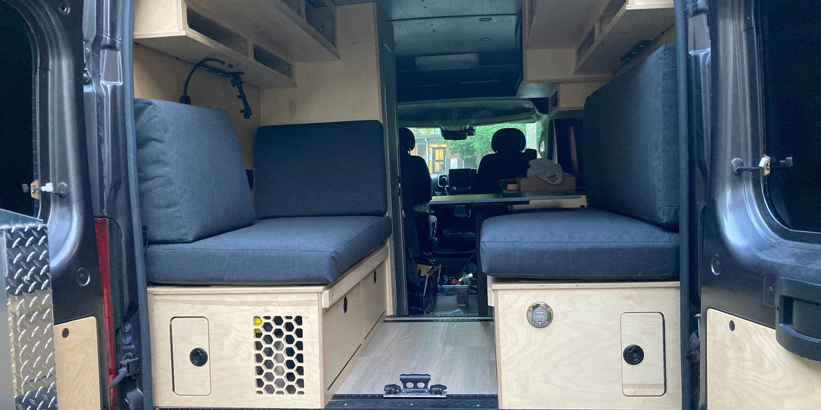 Rear view of a custom 2020 Ram ProMaster 2500 High Roof camper van with handcrafted birch cabinetry, bench seating, upper cabinets, and custom storage by Overland Interiors.