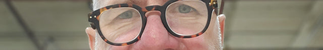 Man wearing glasses and a wine coloured shirt with a blurred background