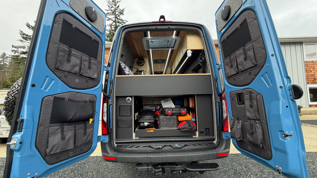 Blue sprinter van with open rear doors showing storage compartments by overland interiors.