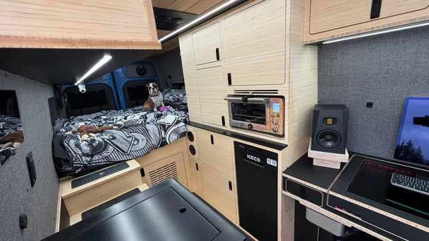 Compact living space with a bed, kitchenette, and electronic devices.