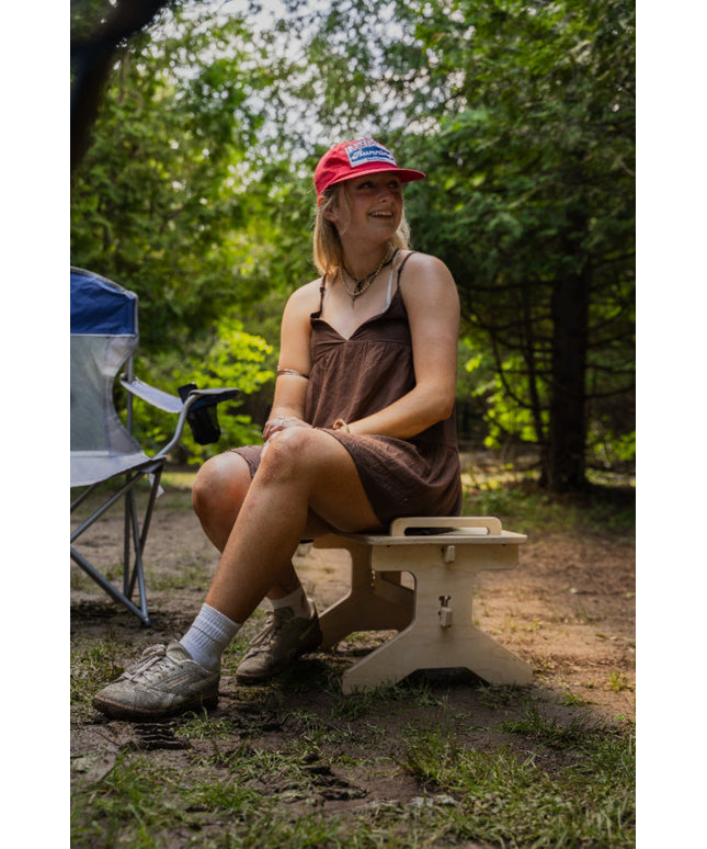 Woman sitting on a portable wooden seat that doubles as step stool in a wooded area