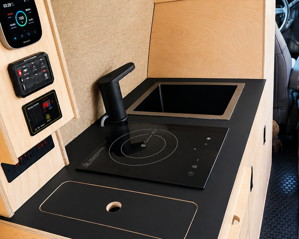 Overland Interiors 36-inch kitchenette in a low-roof van featuring a black countertop, induction cooktop, sink and integrated storage.