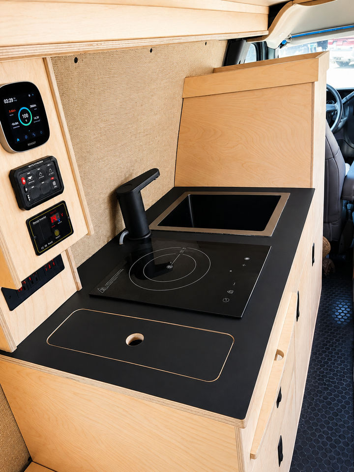 Overland Interiors 36-inch kitchenette in a low-roof van featuring a black countertop, induction cooktop, sink and integrated storage.