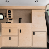 Front view of a 36-inch plywood camper van kitchenette with sink, faucet, electrical control panel, storage drawers, cabinet doors, and a tall utility cabinet in an Overland Interiors Low Roof Van Kit.