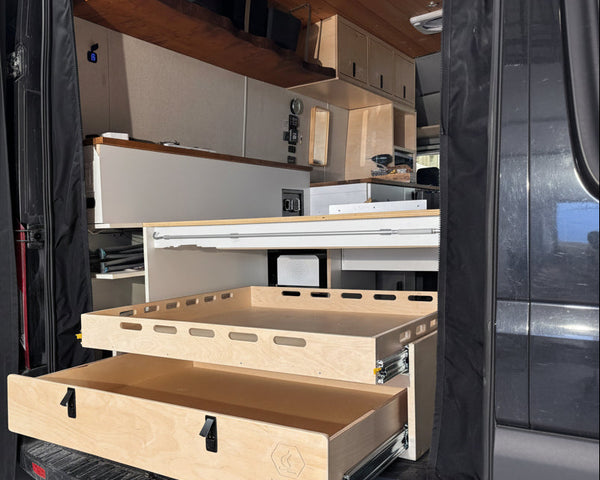 Installed rear pull-out storage drawer system inside a camper van conversion with sliding cargo tray and organized gear storage by Overland Interiors