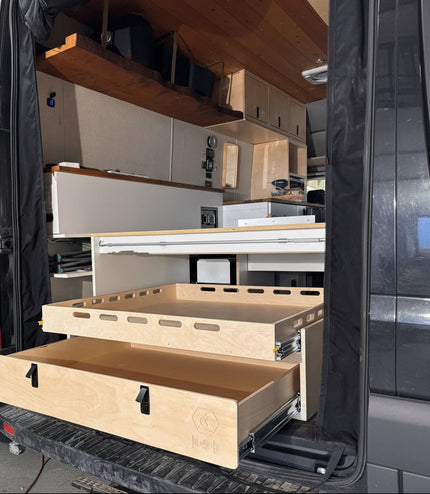 Installed rear pull-out storage drawer system inside a camper van conversion with sliding cargo tray and organized gear storage by Overland Interiors