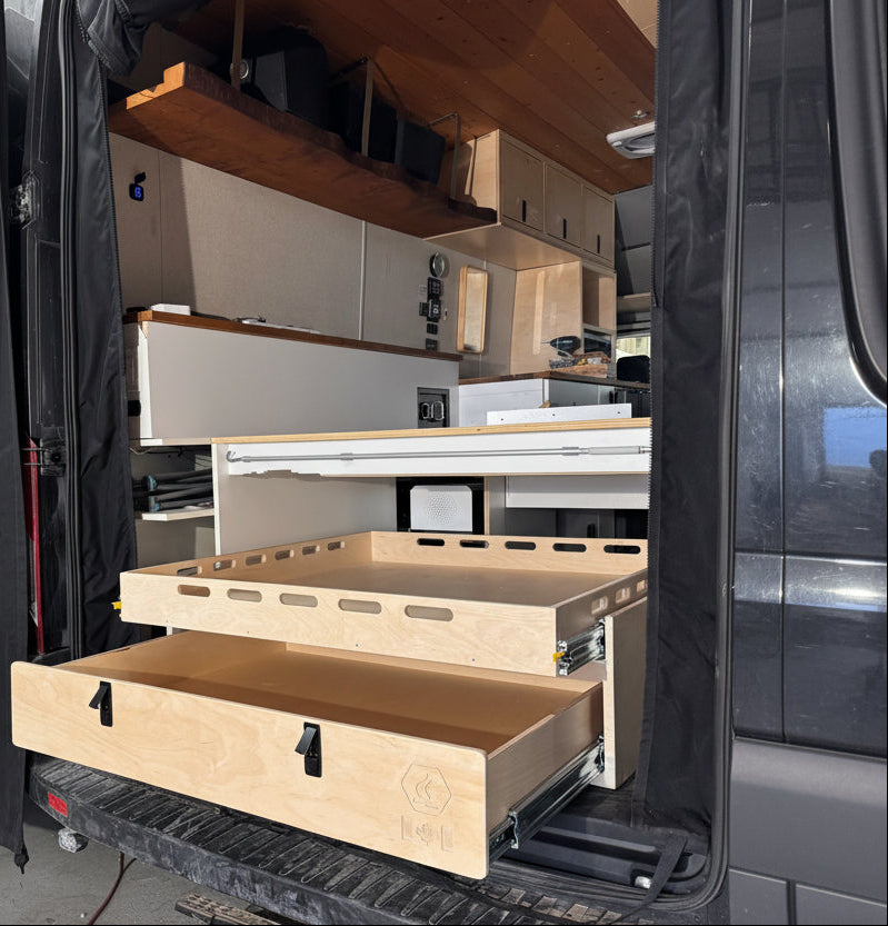 Installed rear pull-out storage drawer system inside a camper van conversion with sliding cargo tray and organized gear storage by Overland Interiors