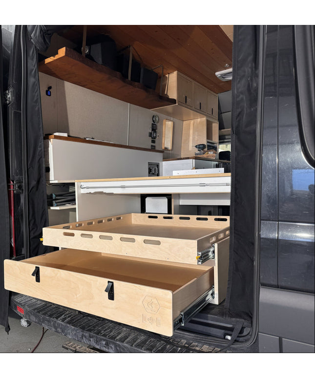 Installed rear pull-out storage drawer system inside a camper van conversion with sliding cargo tray and organized gear storage by Overland Interiors