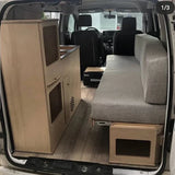 Installed compact camper van kitchenette with integrated sink cabinet and bench seating inside a modular van conversion by Overland Interiors.