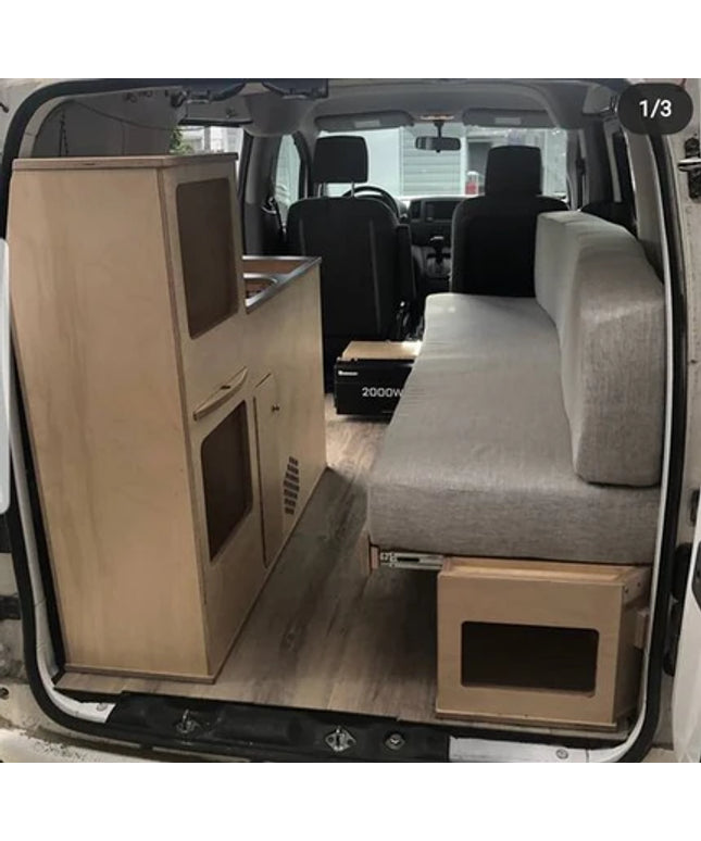 Installed compact camper van kitchenette with integrated sink cabinet and bench seating inside a modular van conversion by Overland Interiors.