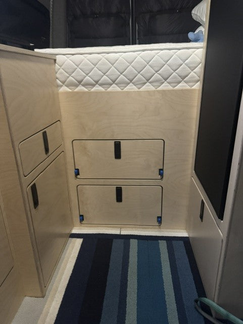 Custom garage access panel with integrated storage doors beneath the raised bed in a Mercedes Sprinter 144 camper van.