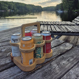 Wooden 6-pack beer carrier holding beverage cans outdoors on a dock by Overland Interiors.