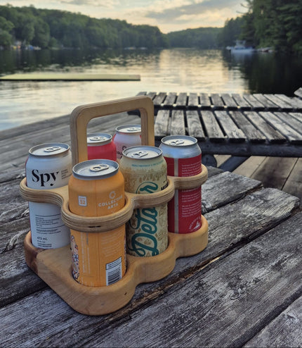 Wooden 6-pack beer carrier holding beverage cans outdoors on a dock by Overland Interiors.