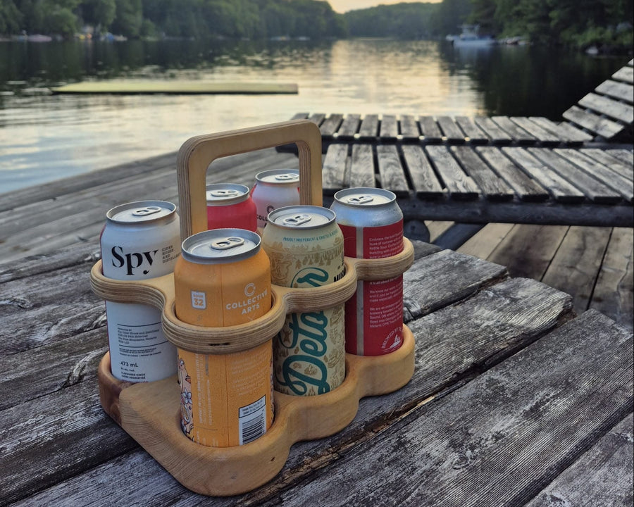 Wooden 6-pack beer carrier holding beverage cans outdoors on a dock by Overland Interiors.