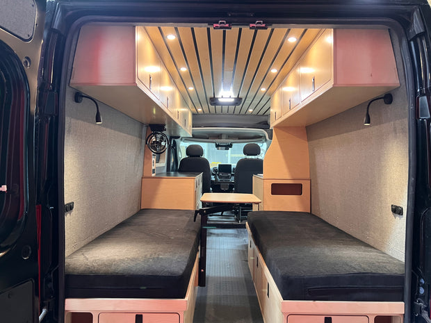 Inside of a van converted into a living space with beds, desk, storage by Overland Interiors