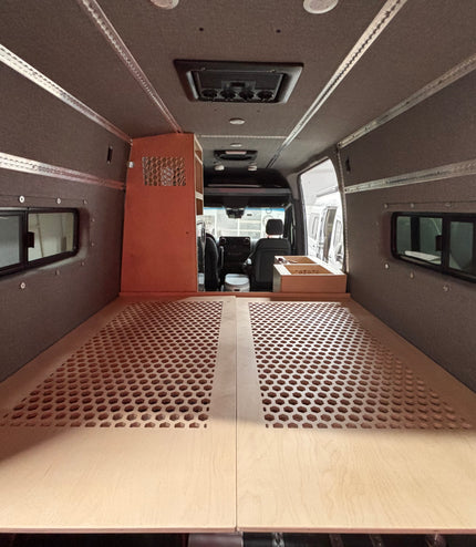 Interior of a van with a wooden bed platform and fabric walls with Ltrack mounts