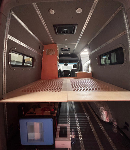 Interior of a van with a bed setup and small kitchen area.