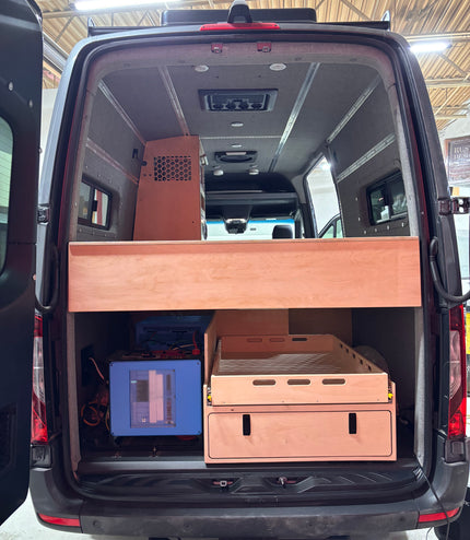 Van interior with wooden storage compartments and electronic equipment.