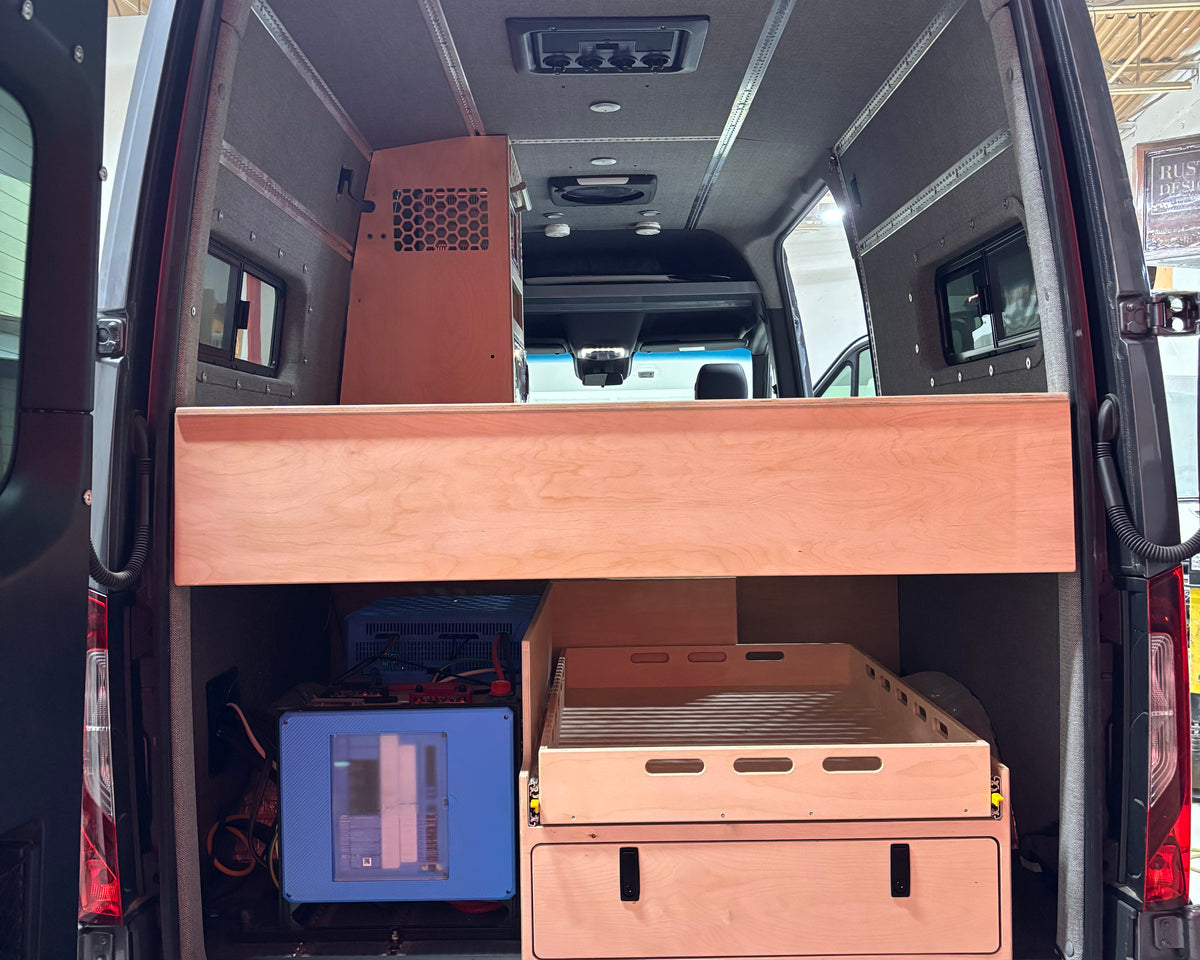 Van interior with wooden storage compartments and electronic equipment.